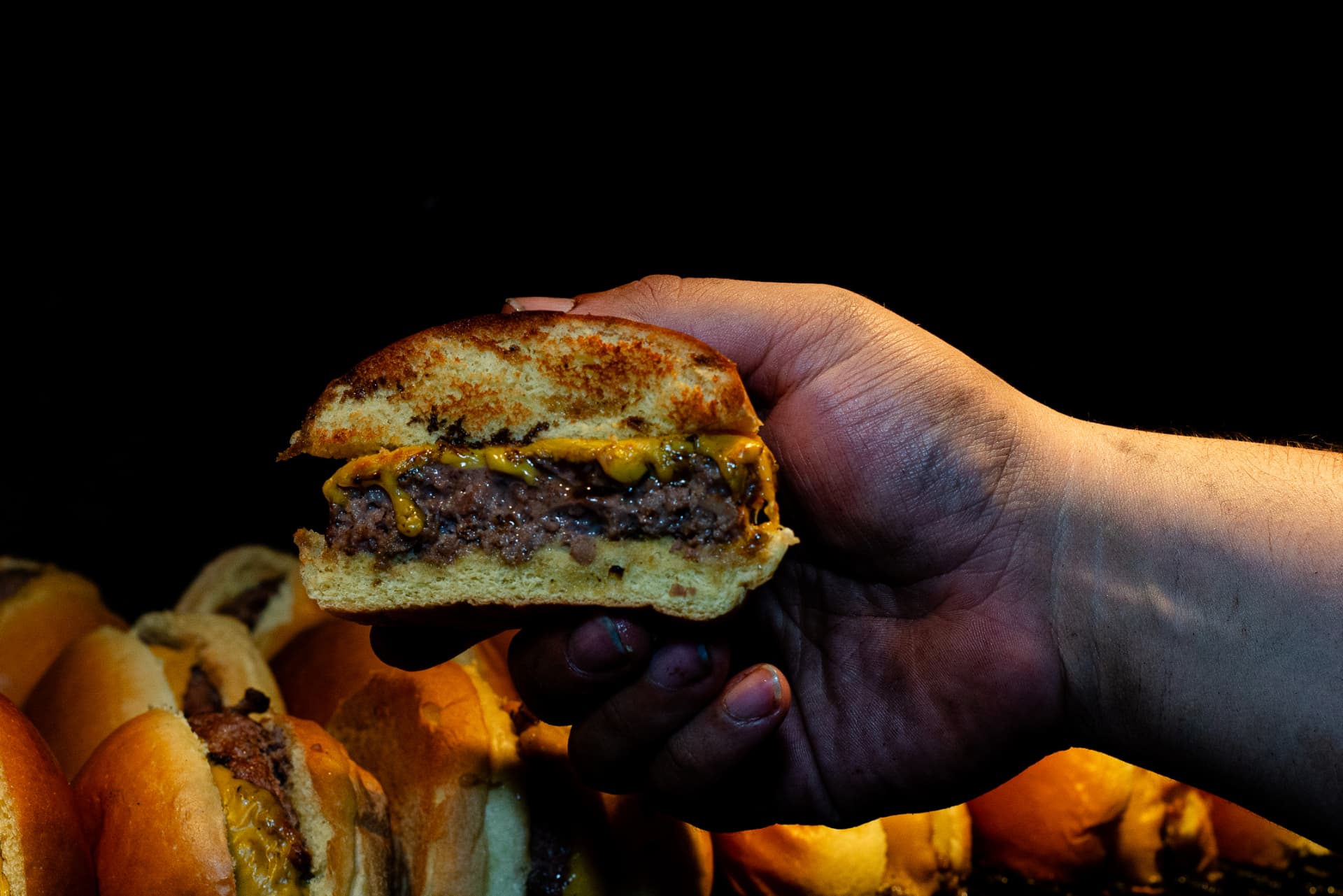 Mão segurando hambúrguer artesanal com queijo derretido feito na brasa